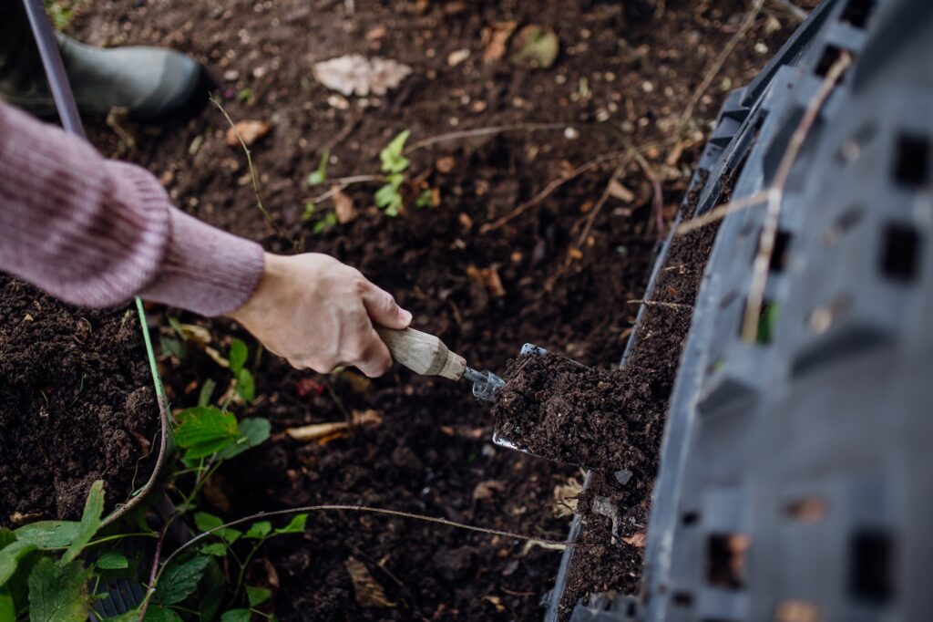 Girl removing compost from a composter in the garden. Concept of composting and sustainable organic